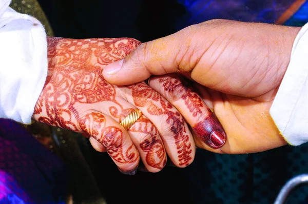 A closeup of a man holding the hand of a female decorated with red mehndi