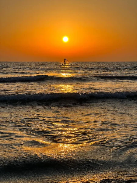 風光明媚な夕日の間にスタンドアップパドルボード上の男の垂直ショット — ストック写真