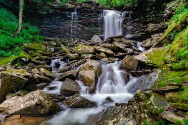 Hills Creek 'in güzel şelalesinin alçak açılı manzarası. Yosun tutmuş kayalar yeşilliklerle çevrili.