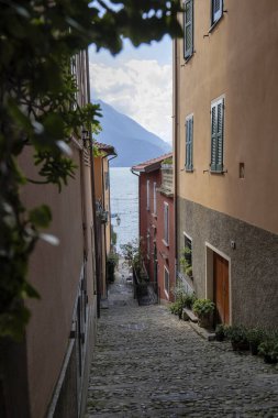 İtalya 'nın Como Gölü' ne giden güneşli Varenna kasabasındaki bir ara sokağın dikey görüntüsü.