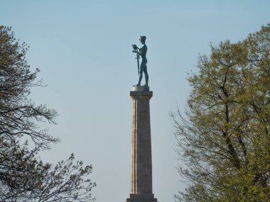Belgrad 'daki uzun Pobednik heykeli Sırbistan' daki ağaçların çerçevesinden