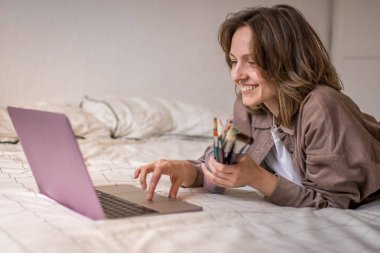 Coşkulu Gülümseyen Kız 'ın fotoğrafı bilgisayarından fırça kavanozuyla Online Derslerle Resim Yapmayı Öğrenmeye Hazırlanıyor
