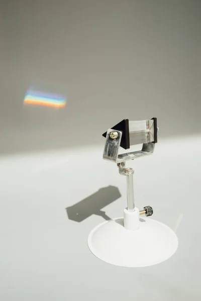 A vertical shot of a prism with a refraction of light into a rainbow on a gray wall