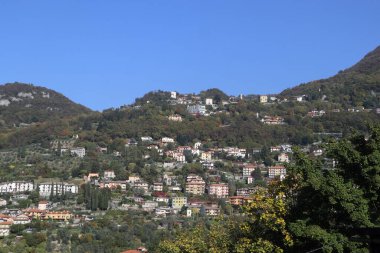 Mavi gökyüzünün altındaki ağaçlarla çevrili konutlar.