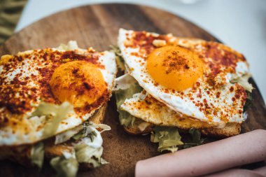 Kızarmış ekmeğin yakın plan çekimi. Üstünde marul ve kırmızı biberli sahanda yumurta var.