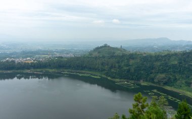 Bulutlu bir gökyüzünün altındaki ağaçlarla çevrili sakin bir göl manzarası.