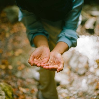 Bulanık bokeh arka planda bir insanın açık avuçlarının su ile sığ odak görüntüsü