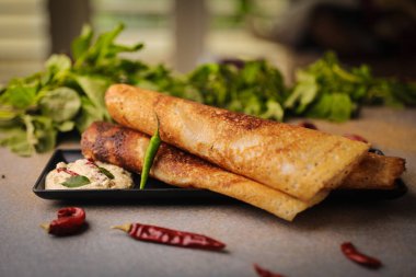 Geleneksel Hint yemeği Dosa 'nın yakın çekimi. Ahşap masadaki bir tabakta sos var.