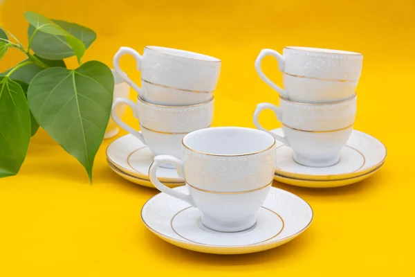 White porcelain tea cup with a golden line decoration on yellow colour background.