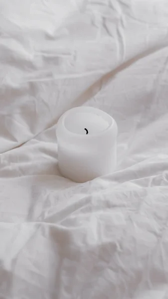 A closeup shot of a small white candle on a white bed sheet