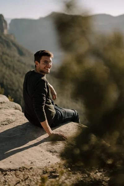 一个西班牙裔男子坐在一块巨大的岩石上看着摄像机的垂直照片 — 图库照片