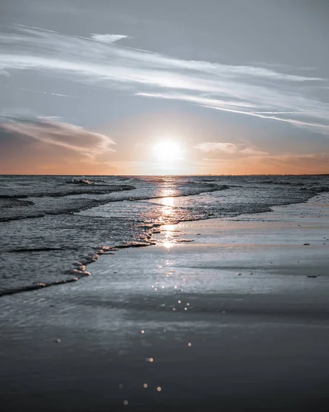 A vertical shot of the sun setting on the horizon of the ocean with calm waves in color splash