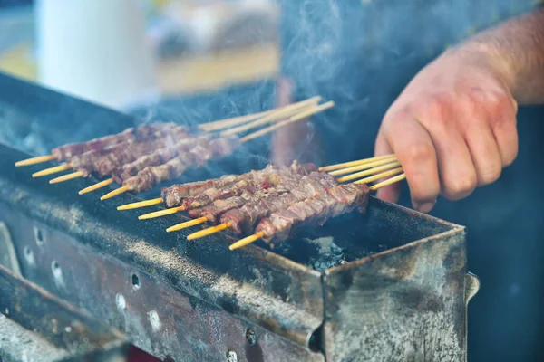 烤肉人的手 手握着烤肉架上烤的羊肉串 — 图库照片