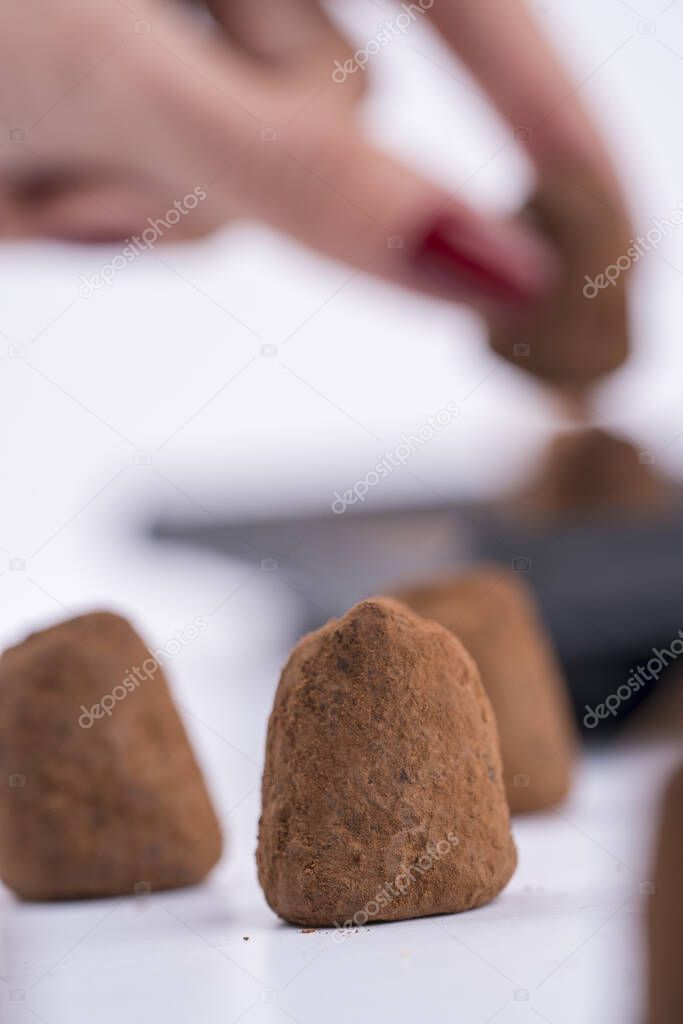 A vertical selective focus shot of a woman's hand lining up truffles on a shite table