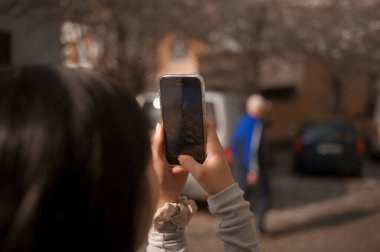 Sokakta akıllı bir telefonla fotoğraf çeken genç bir kadının arka görüntüsü.