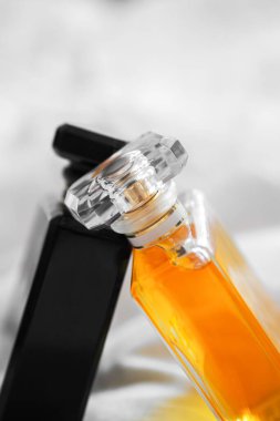 Bulanık arka planda beyaz bir çarşaf üzerinde iki parfüm şişesinin dikey çekimi.