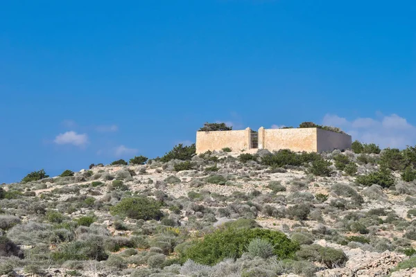 Garigue landscape of the island of Comino in Maltese Islands, and the outer wall of the cemetery on the island, used for isolated sick patients