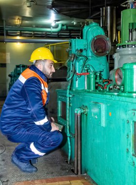 Kafasında kaskla yanındaki makineyi izleyen bir işçinin dikey görüntüsü.