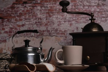 Süt sürahisi, öğütücü ve şekerli ahşap kaşıklar ve tuğla duvar zeminli ahşap bir masada öğütülmüş kahve.