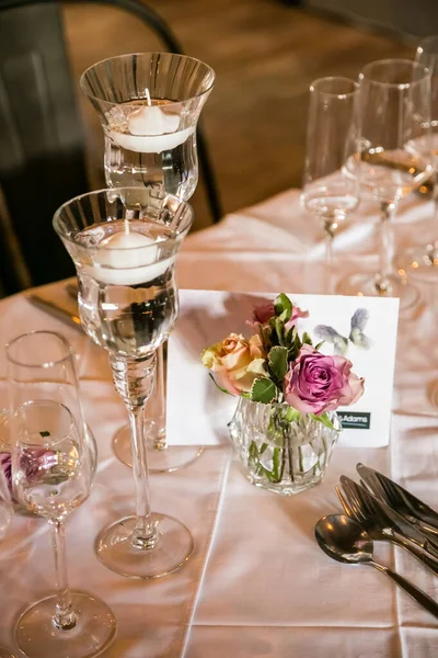 A vertical shot of glasses and flowers on the table with a white tablecloth