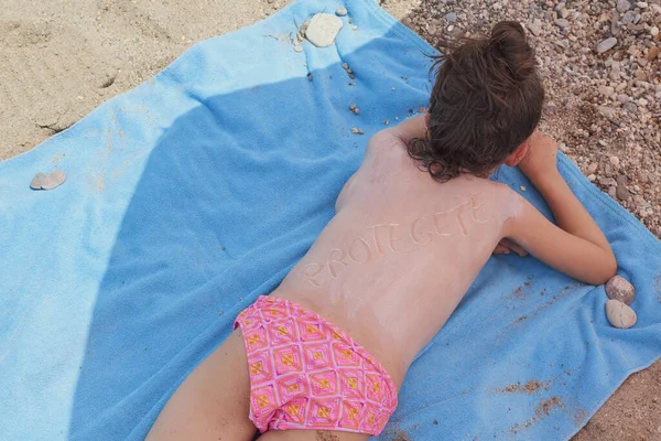 Дівчинка Лежить Своєму Блакитному Рушнику Словом Захист Написаним Вершками Пляжі — стокове фото