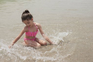 Pembe bikinili kız güneşli bir yaz gününde kumsalda dalgalarla mutlu mesut oynuyor, Vera, İspanya