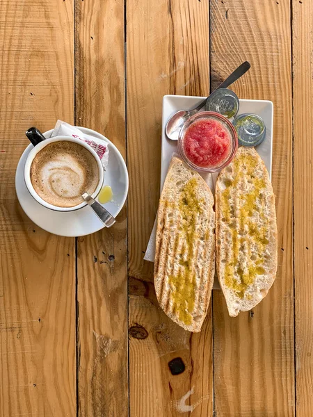 A wooden pallet table with a cup of coffee, toasted bread, crushed tomato, olive oil and salt