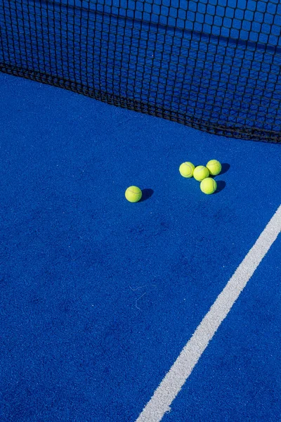 A vertical shot of paddle tennis balls by the net on a blue paddle tennis court