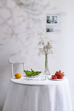Dikey bir sandalye ve meyve dolu bir masa ve arka planda beyaz bir duvar vazosu.