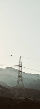 Kırsal kesimde, arka planda dağlar olan bir iletişim kulesinin dikey görüntüsü.