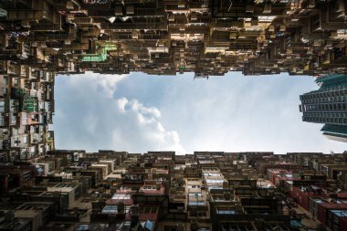 Bulutlu bir gökyüzüne karşı balkonları olan yüksek bir binanın alt görüntüsü.