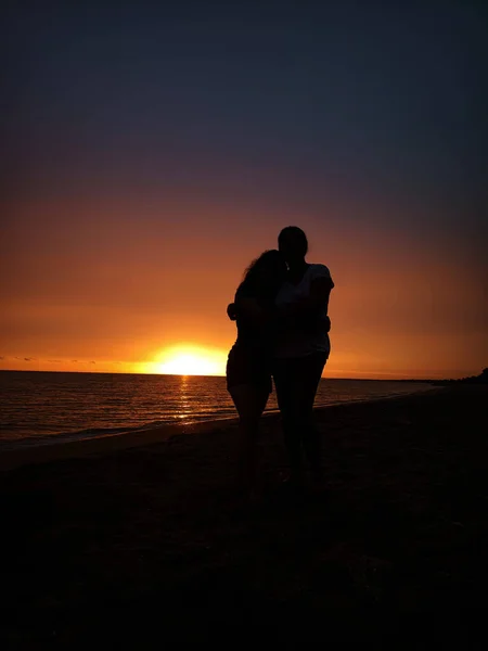 A silhouette vertical shot of a couple hugging one another by the sea at sunset - concept of romance