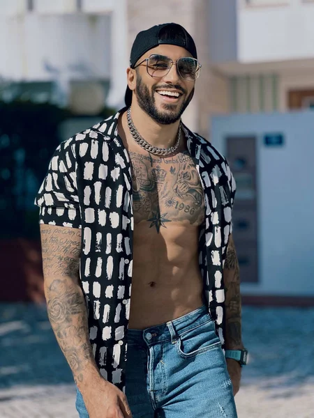 The vertical shot of a male adult tattooed  model wearing sunglasses and smiling at a camera