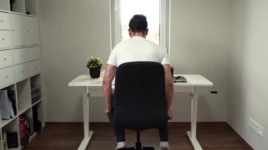 Masasında otururken bilgisayarda çalışan yetişkin bir erkek.