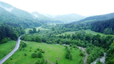Kırsal alanda, arka planda dağlar olan tarlalardan geçen bir yolun hava aracı görüntüsü.