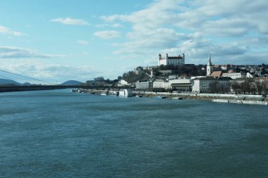 Bulutlu gökyüzünde gölün yanındaki tepede bir kasaba..