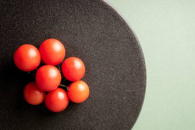 Yeşil arka planda siyah plaka üzerinde küçük domateslerin üst görüntüsü