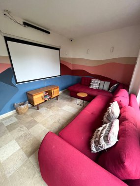 Proje ekranı, ses çubuğu, büyük koltuklar, yastıklar, rahat koltuklar, pembe ve mavi duvar tasarımları olan rahat bir ev sinema odası.
