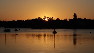 Siluetli tekne ve ağaçlarla dolu bir nehrin gün batımı manzarası