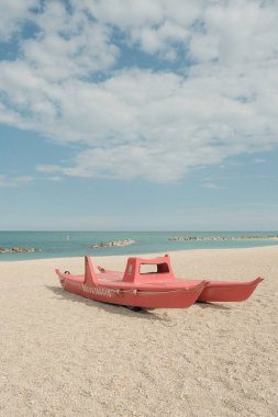 Sabah kumlu bir sahilde kırmızı bir tekne.