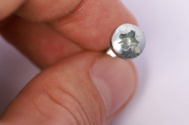 Beyaz arka planda metalik yuvarlak bir vidayı tutan bir elin yakın çekimi.