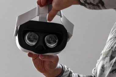 Beyaz bir duvar arkasında sanal gerçeklik kulaklığı tutan bir adam.