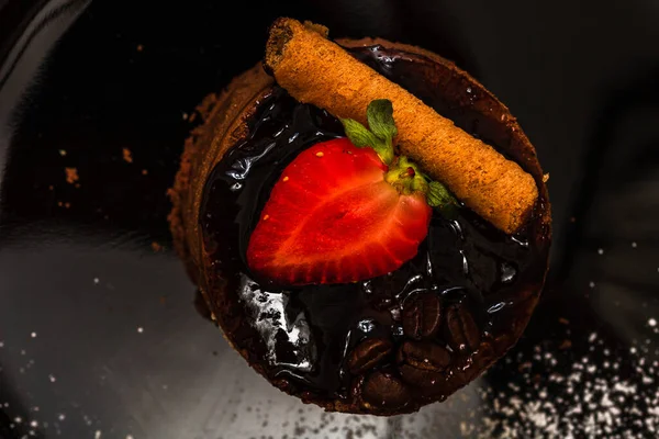 A top view of a chocolate mousse cake with strawberry and chocolate stick on a black plate