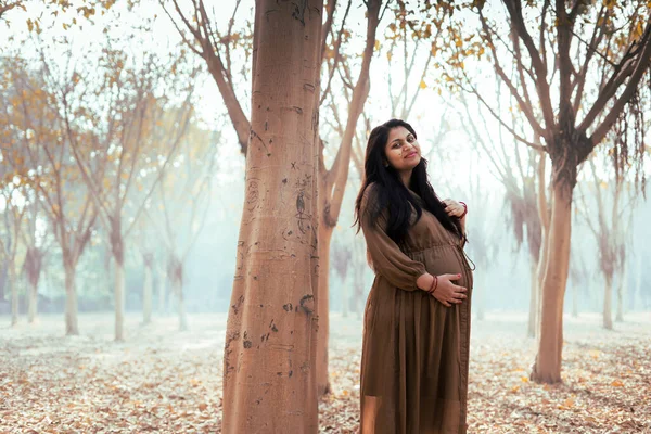 一个年轻美丽的怀孕女子在公园里摆姿势 抱着她的肚子 — 图库照片