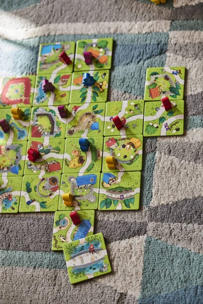 A vertical of the Carcassonne Junior game with cards and colorful wooden figurines on a carpet