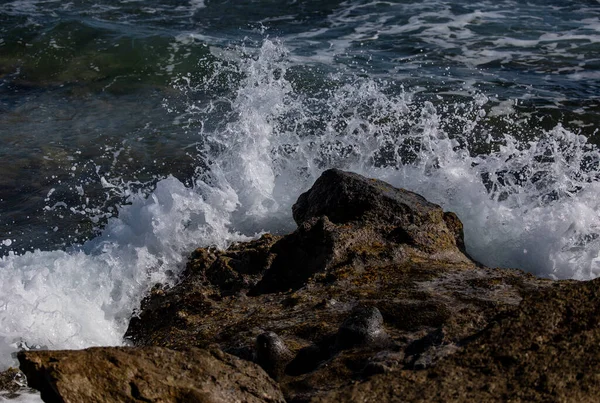 在一个阳光明媚的日子里 一个美丽的浪花拍打在海滩上的一块大石头上 — 图库照片