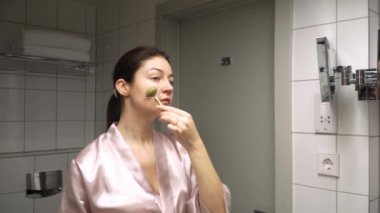 Genç bir dişi, gece kendi kendine bakım rutinini yapıyor. Yüzüne banyoda taş bir silindirle masaj yapıyor.