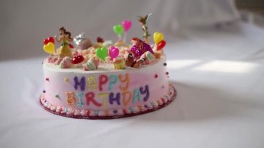 Beyaz masa örtüsü üzerinde pembe bir pasta ve küçük oyuncak figürlerinin görüntüleri. İyi ki doğdun.