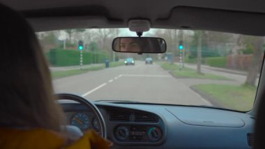 Groningen şehrinde, trafik lambaları ve okul bölgesinden geçen yaşlı araba kullanan genç bir kadın.