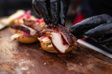 Bir şefin elleri ahşap bir masada iştah açıcı bir burger hazırlıyor.